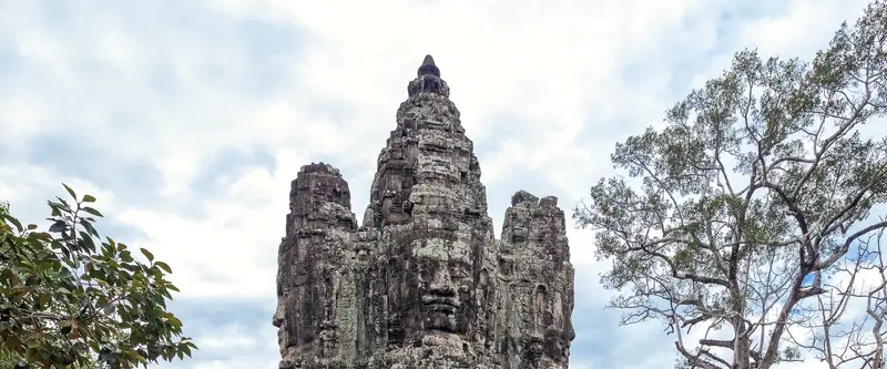 tour à visages de pierre d'une porte d'Angkor Thom, encadrée par les arbres