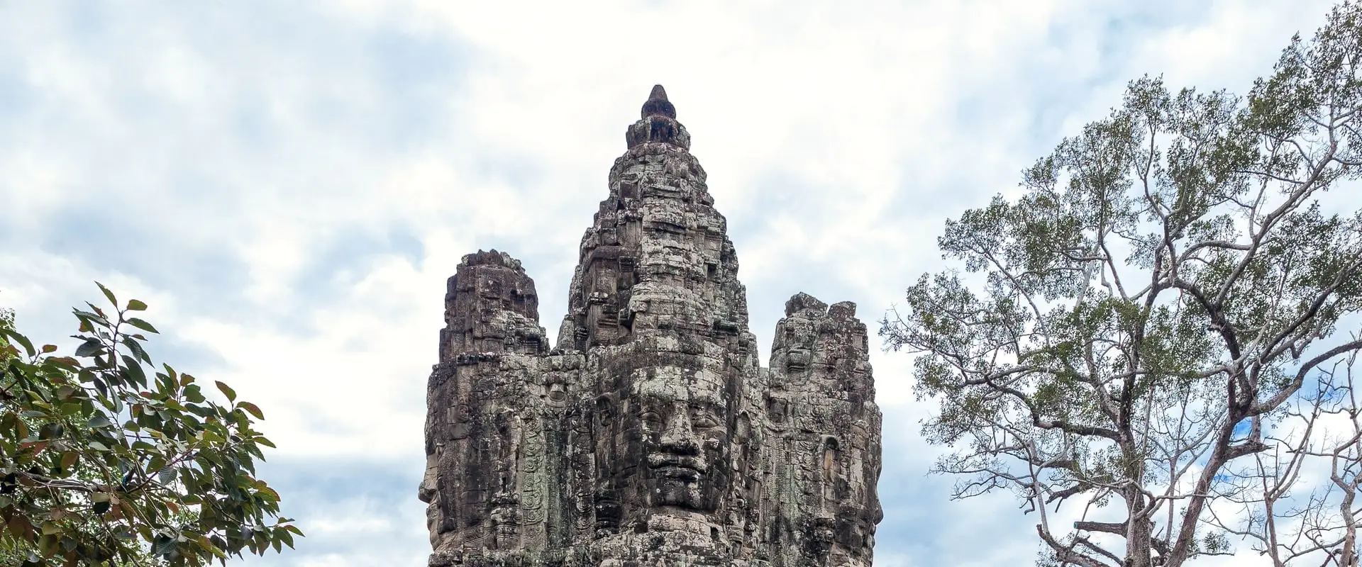 tour à visages de pierre d'une porte d'Angkor Thom, encadrée par les arbres
